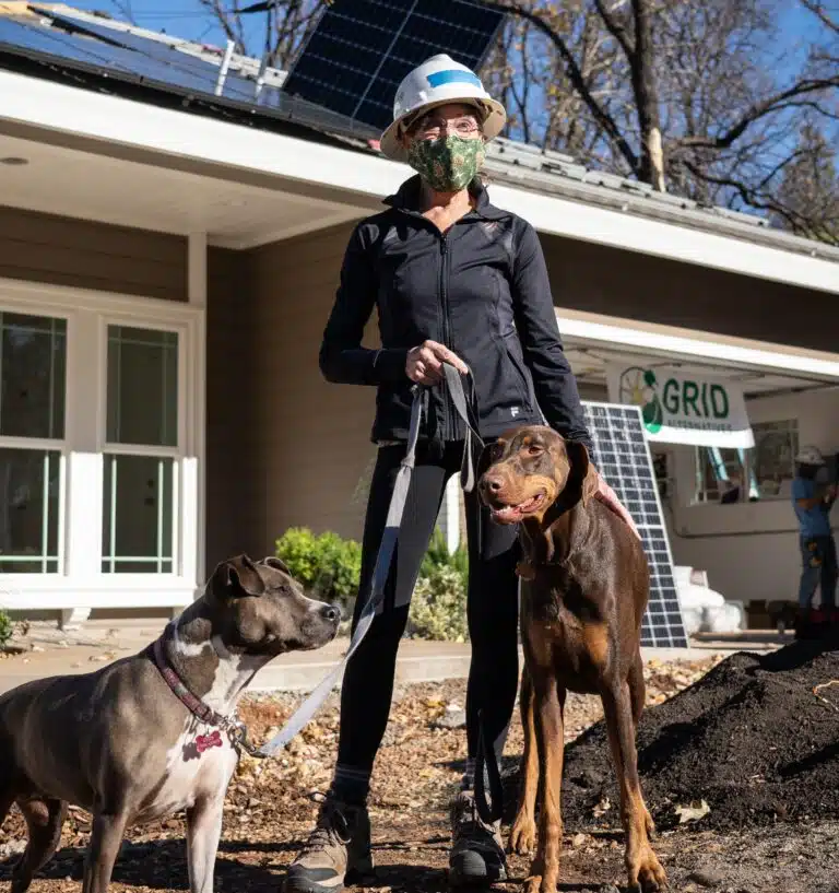 Woman in hard hat and mask with two dogs at solar panel installation site