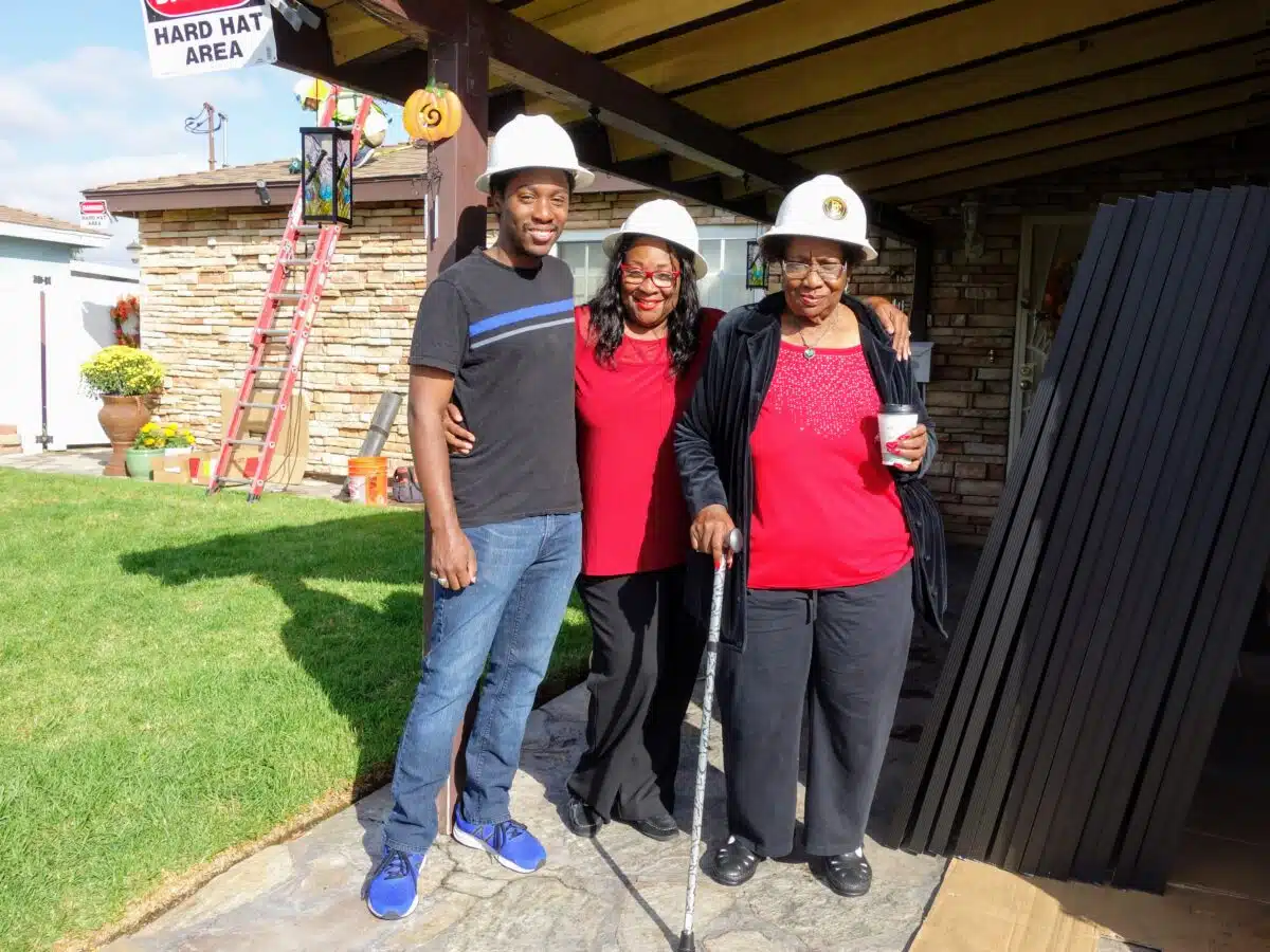 Three people wearing white hard hats stand together on a home patio during a construction or renovation project