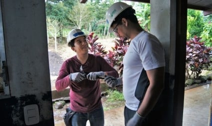 Two men wearing caps converse in a doorway with tropical plants visible in the background