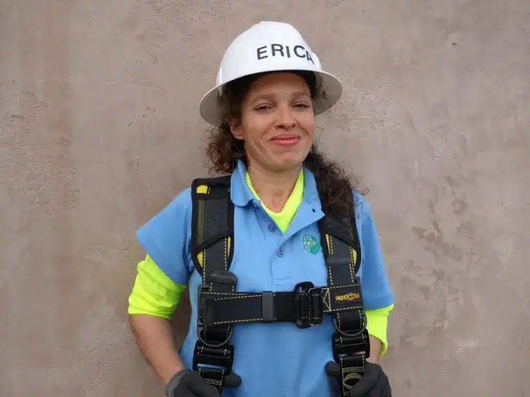 Woman in safety gear with "ERICH" hard hat and harness smiling at camera