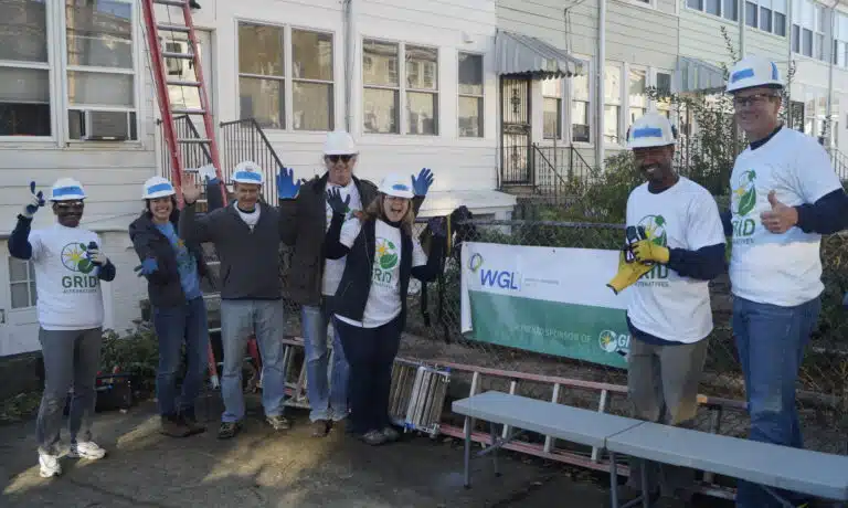 Community volunteers in hard hats and GRID t-shirts hold WGL sponsor banner at outdoor worksite