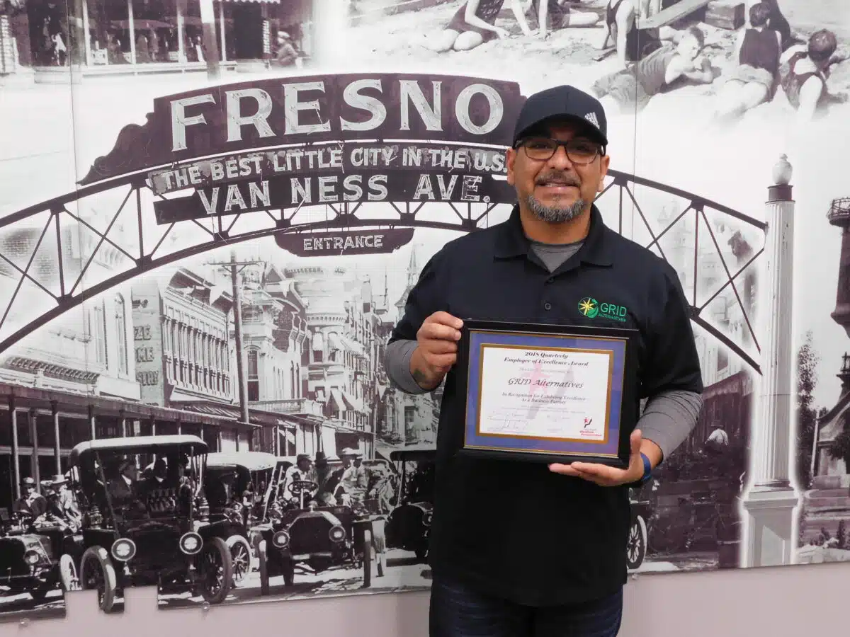 Man holding award certificate in front of Fresno Van Ness Ave vintage mural