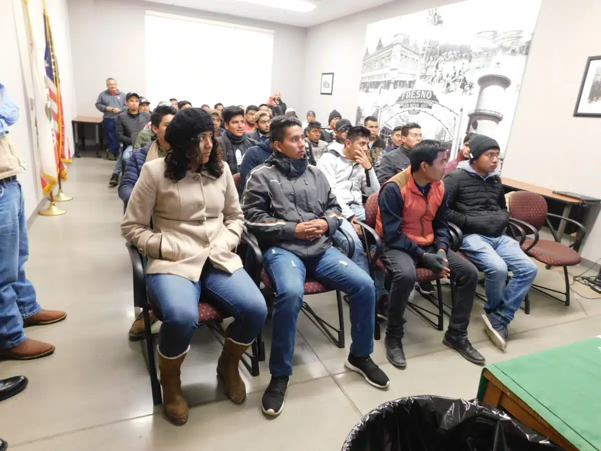 Group of people seated in a community meeting room with an American flag and Fresno historical poster visible