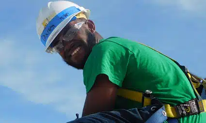 Construction worker in safety gear and hard hat, viewed from below against blue sky