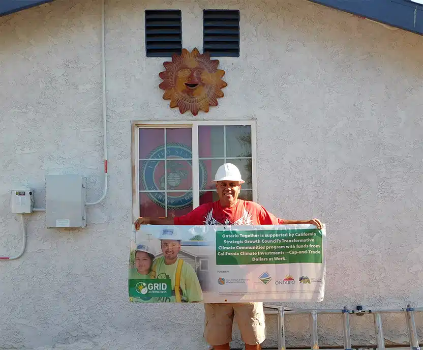 Construction worker holding GRID climate initiative banner in front of building with sun decoration