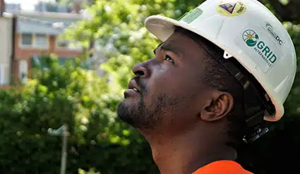 Male worker wearing white hard hat with GRID logo, looking upward outdoors