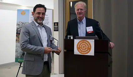 Two men at podium with Rotary logo; man on left holds award plaque