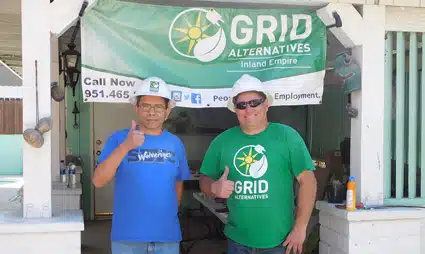 Two men standing in front of GRID Alternatives storefront, one wearing blue shirt, one wearing green GRID shirt