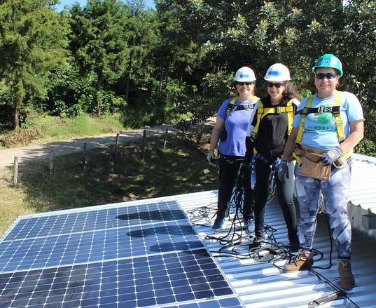 Three people in safety gear stand beside solar panels at El Regadío, Nicaragua installation site