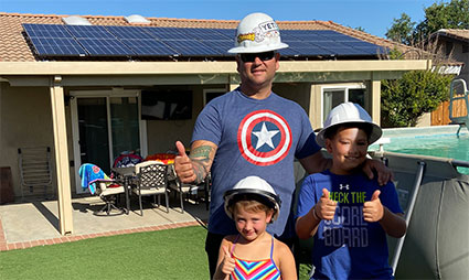 Man and three children wearing hard hats in front of house with solar panels