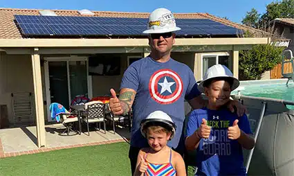 Man and three children wearing hard hats in front of house with solar panels