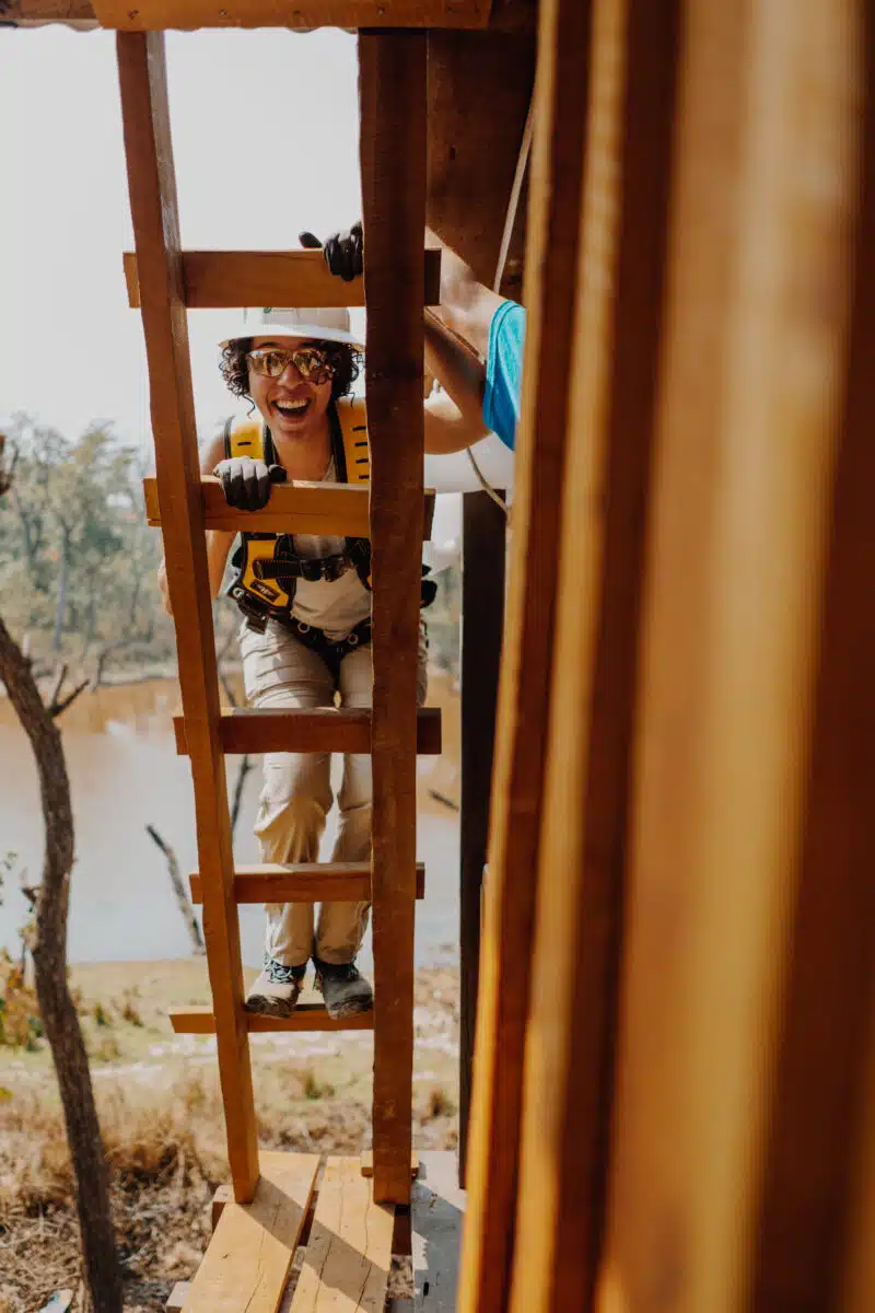 Woman climbing wooden ladder while wearing safety gear and harness