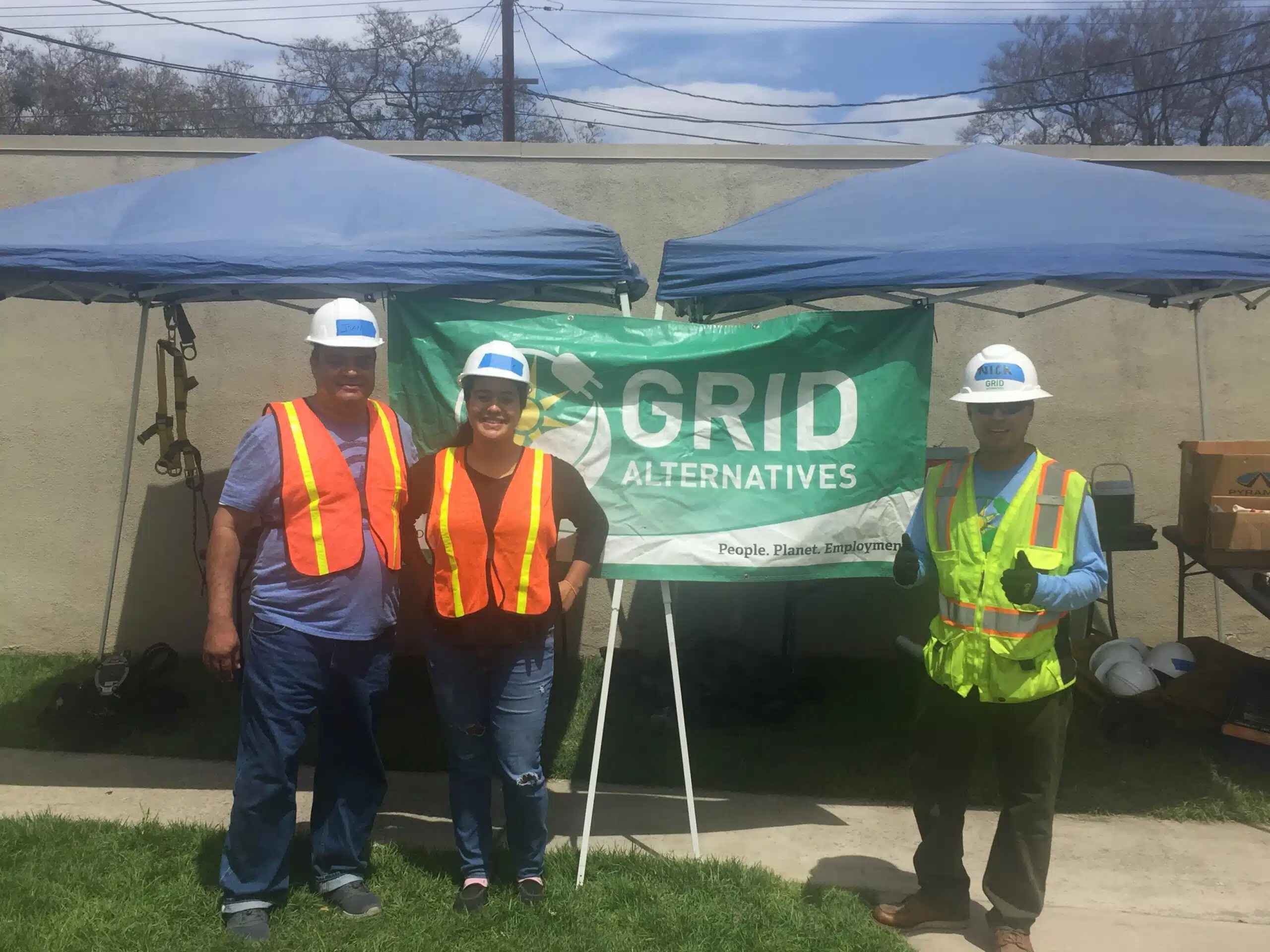 Two family members who are dressed like they are finishing a day as solar trainees stand next to a construction worker in GRID Alternatives gear