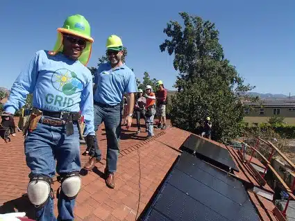 GRID staff in hard hats smile next to a newly installed rooftop solar array.