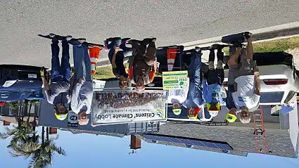 Eight people in Citizens' Climate Lobby, a group concerned about the quality of air we breathe, stand with a GRID Alternatives sign in front of a house where the GRID Solar Installation Supervisor has been training them