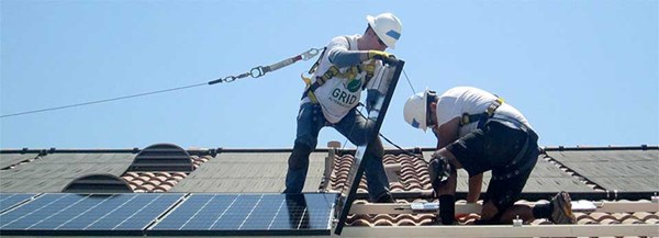 Two workers installing solar panels on a residential roof under clear sky