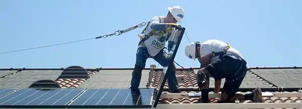 Two workers installing solar panels on a residential roof under clear sky