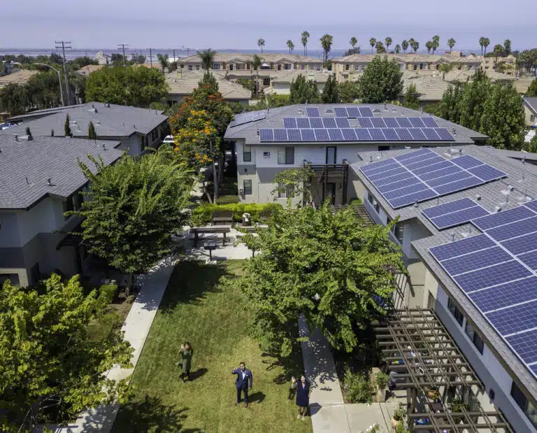 Aerial view of modern homes with solar panels on roofs in a suburban neighborhood with green trees and landscaping