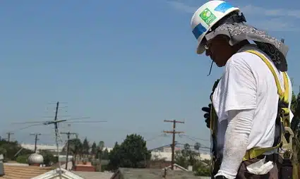 Construction worker in safety helmet and harness on rooftop surveying job site