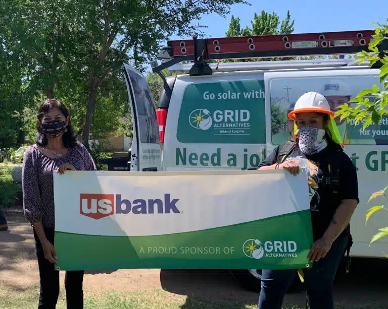 Two people holding US Bank banner in front of GRID Alternatives solar van