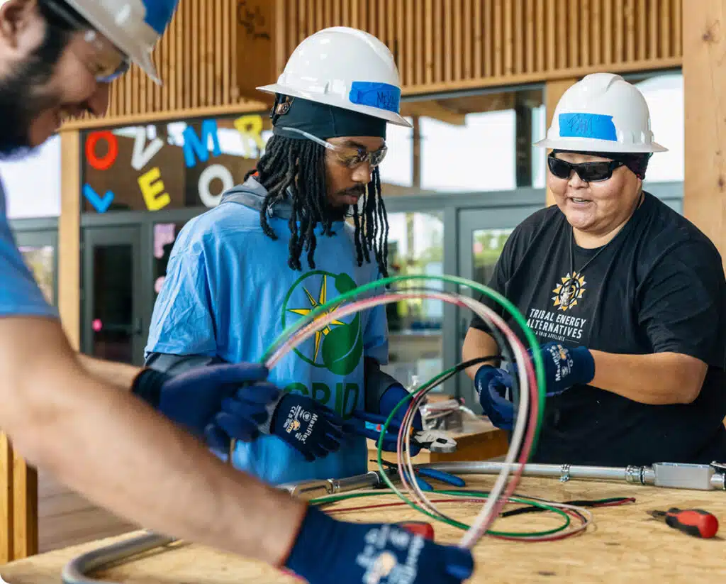 Instructors and students examine electrical wiring and cables during a hands-on renewable energy training class