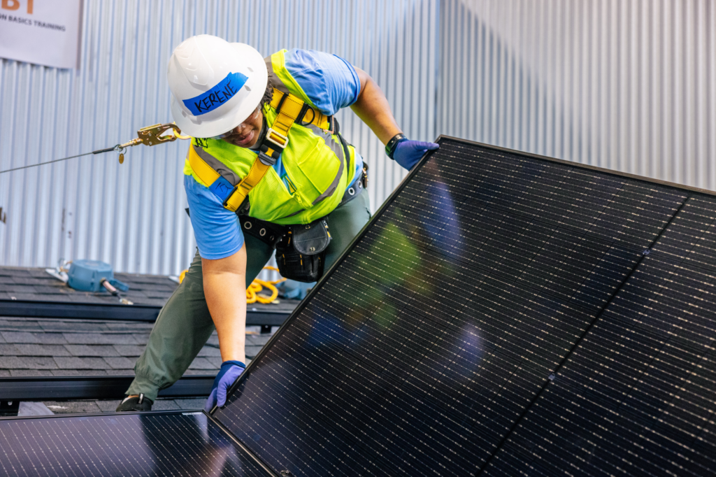 Worker installing solar panel on roof wearing safety harness and hard hat
