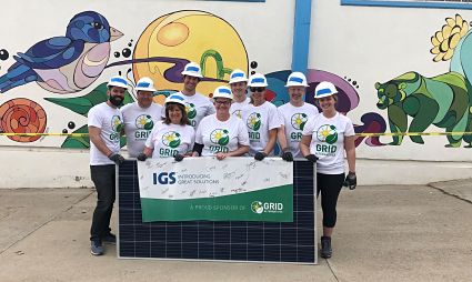 Team of eight people in white shirts holding IGS banner in front of colorful mural