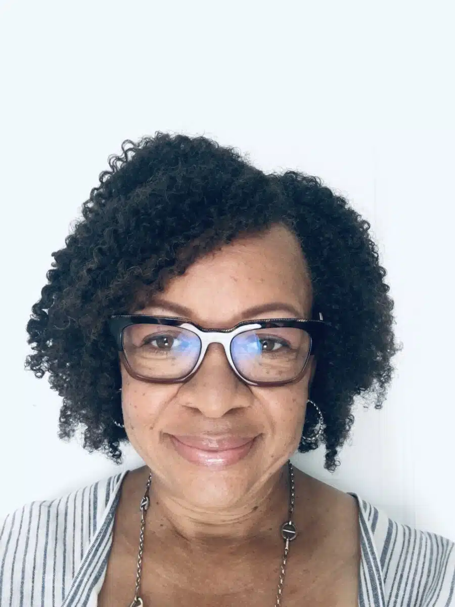 A person with curly dark hair and glasses smiles in a profile picture