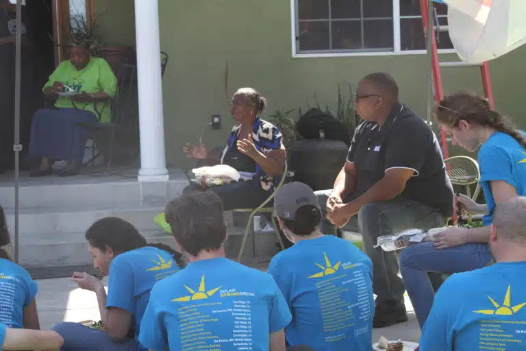 Group of people wearing blue Solar Springbreak t-shirts seated outdoors listening to speakers at an event