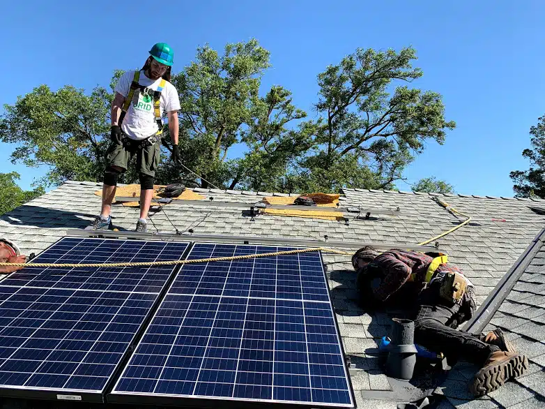 Two workers installing solar panels on a residential roof under clear blue sky