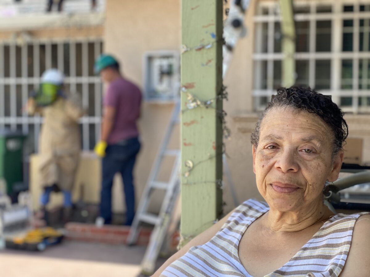 Ms. Audrey in her backyard as GRID staff and solar job trainees work on her solar installation.