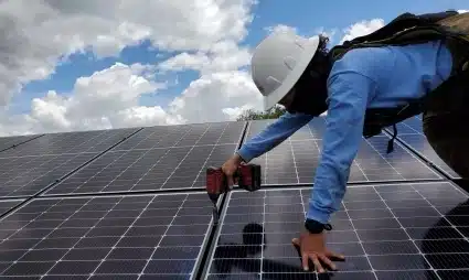 Worker in hard hat installing solar panels on rooftop under cloudy sky