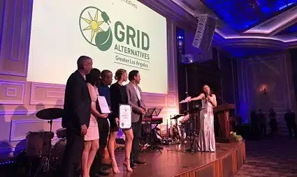 Panel discussion at GRID Alternative conference with five speakers on stage and blue stage lighting