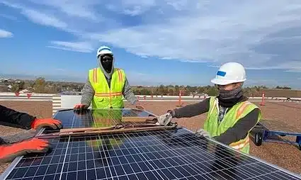 Two workers in safety gear installing solar panels in a field on a sunny day