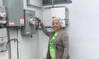 Woman pointing at electrical meter panel on white wall, wearing green lanyard