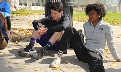 Two young people sitting outdoors examining a prosthetic leg or foot device together