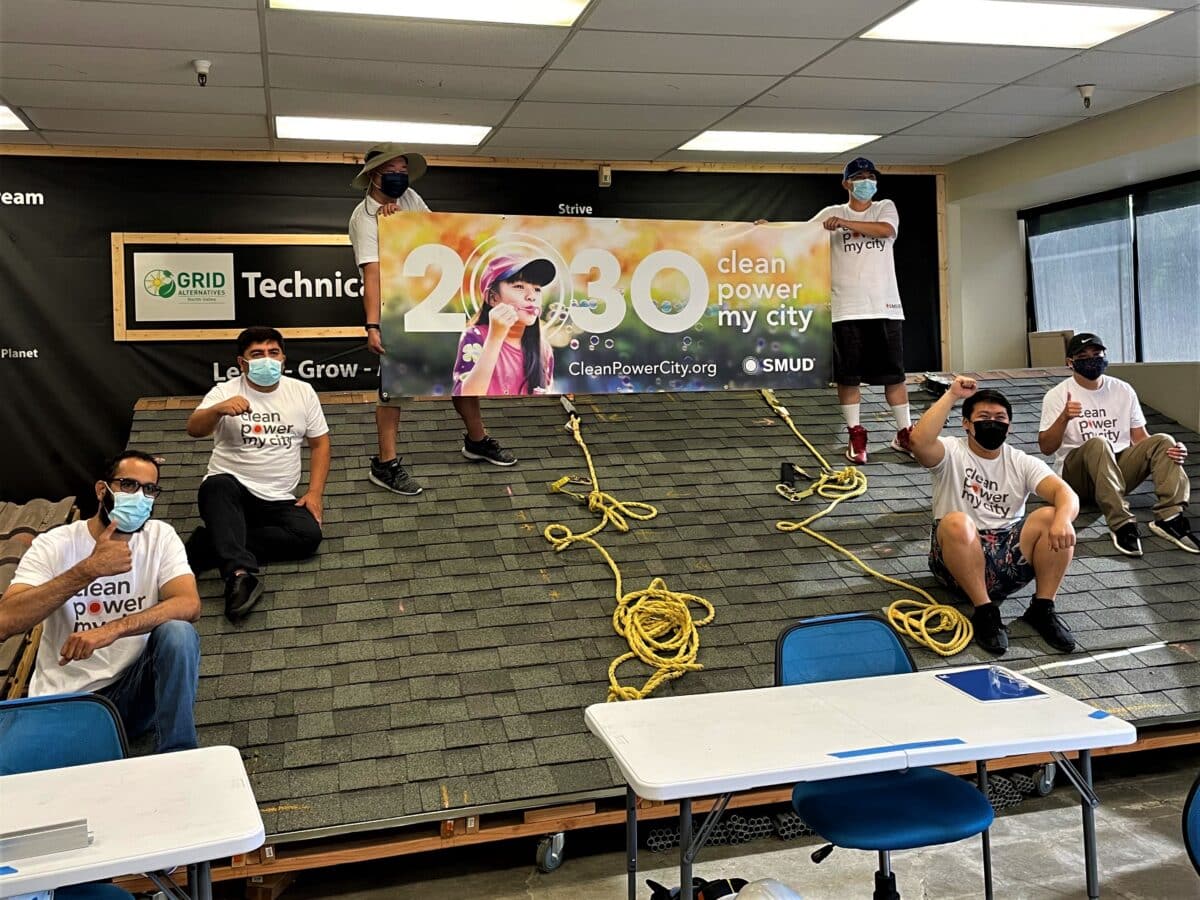 Group of volunteers in "Clean Power My City" shirts indoors with yellow ropes and 2030 banner visible