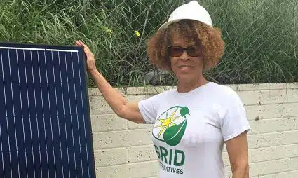 Person holding solar panel wearing GRID Alternatives t-shirt and white cap