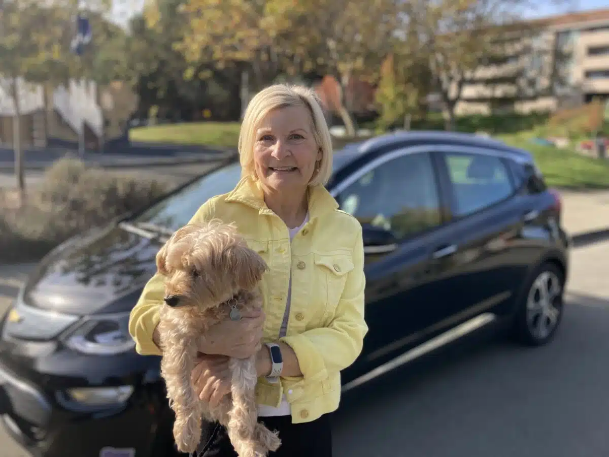 Clean Mobility Program beneficiary is standing next to her recently purchased electric vehicle