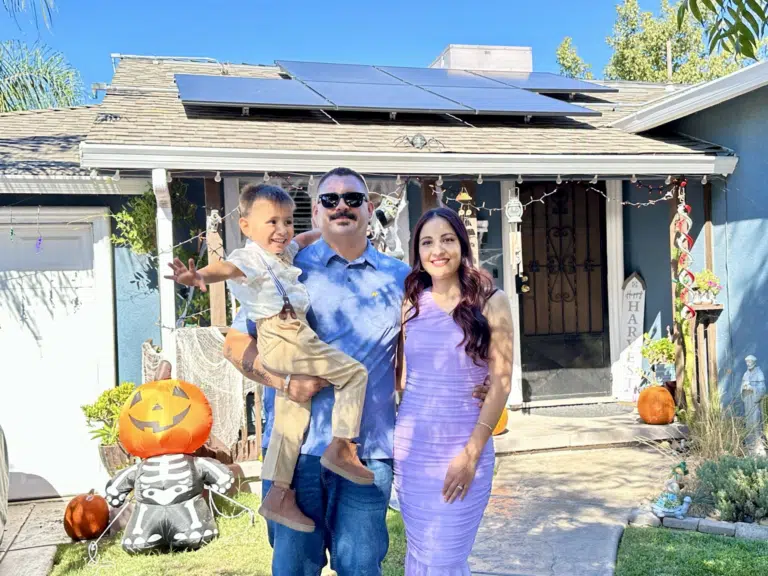 GRID NV client Christian Romo and his wife and son in front of their home with solar panels visible behind them.
