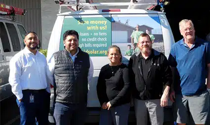 Five people standing in front of a solar panel van with "Save money with us" text visible on the side