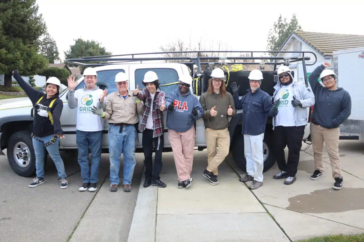 Ten workers in hard hats posing in front of a service van, giving thumbs up and waving at the camera