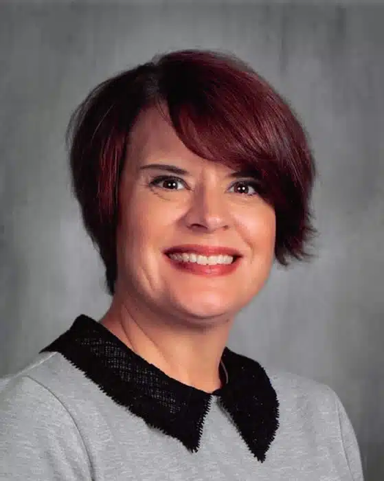 Professional headshot of Janine Medina, woman with burgundy hair and black collar detail, smiling at camera