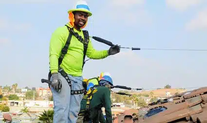Construction worker in safety gear on rooftop with power drill and equipment