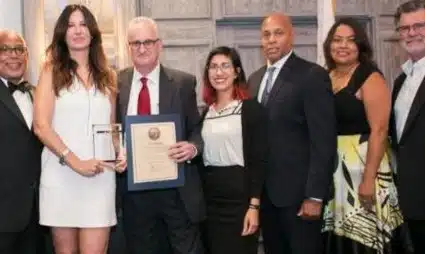 Seven people in formal attire posing together, one holding a framed award certificate