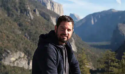 Man smiling at camera with mountain valley and cliffs in background