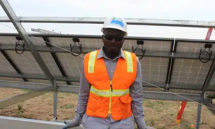 Construction worker in safety gear standing in front of solar panels at community solar farm