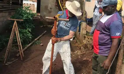 Two men working with soil and tools in a residential outdoor space, one wearing a blue shirt and hat