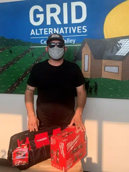 Portrait of Juan, in front of the GRID CV mural, holding the tools he earned