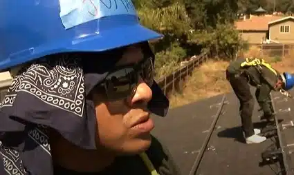 Person wearing blue hard hat and bandana operating roofing equipment outdoors